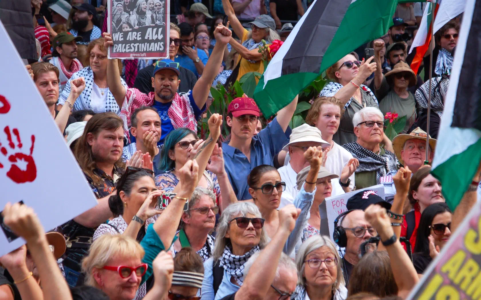 A crowd gathers at Sydney Town Hall with Palestinian flags, placards and arms raised.