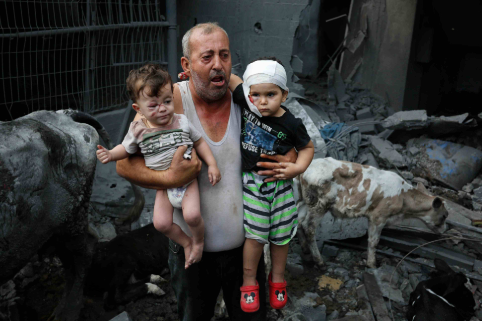 A Palestinian refugee carries his injured grandchildren from the Israeli bombing of Nuseirat Camp, Gaza Strip.