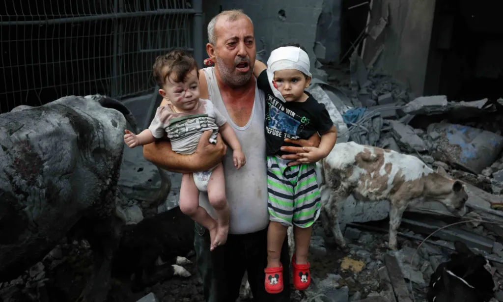 A Palestinian refugee carries his injured grandchildren from the Israeli bombing of Nuseirat Camp, Gaza Strip.
