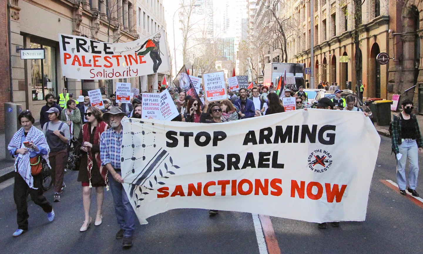 The protest tour marches down a Sydney street holding banners that say "Free Palestine" and " Stop arming Israel, sanctions now".