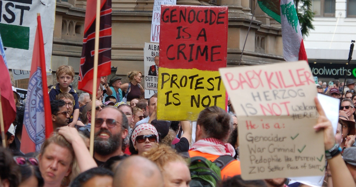Protestors at the Herzog rally in Sydney hold up placards. One reads 'Genocide is a crime. Protest is not.'.